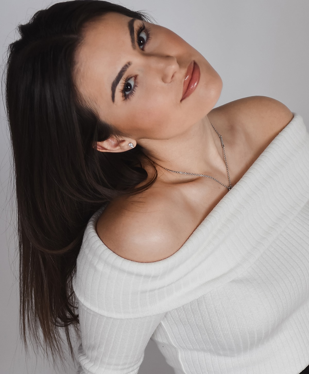 Woman in off-shoulder white top, elegant pose.