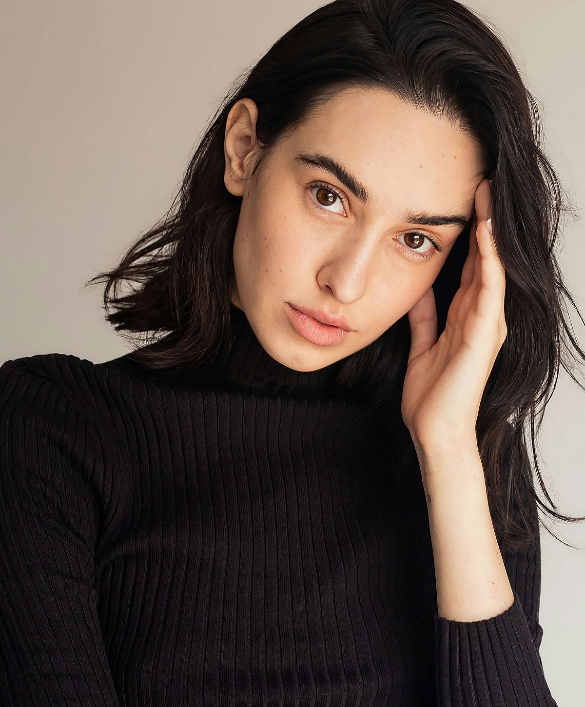 Model posing with hand on head, neutral background.