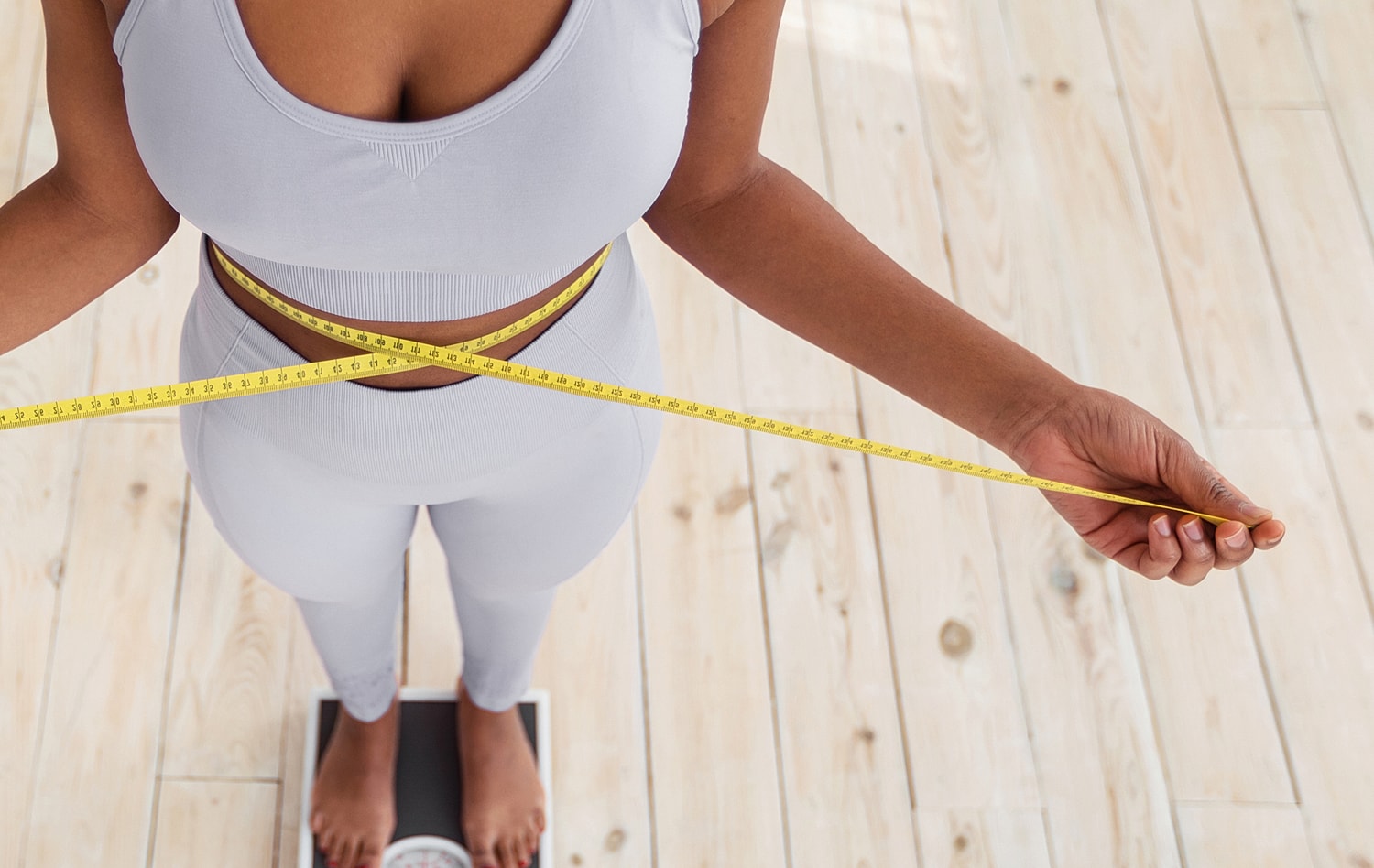 Measuring waist with tape measure on scale.