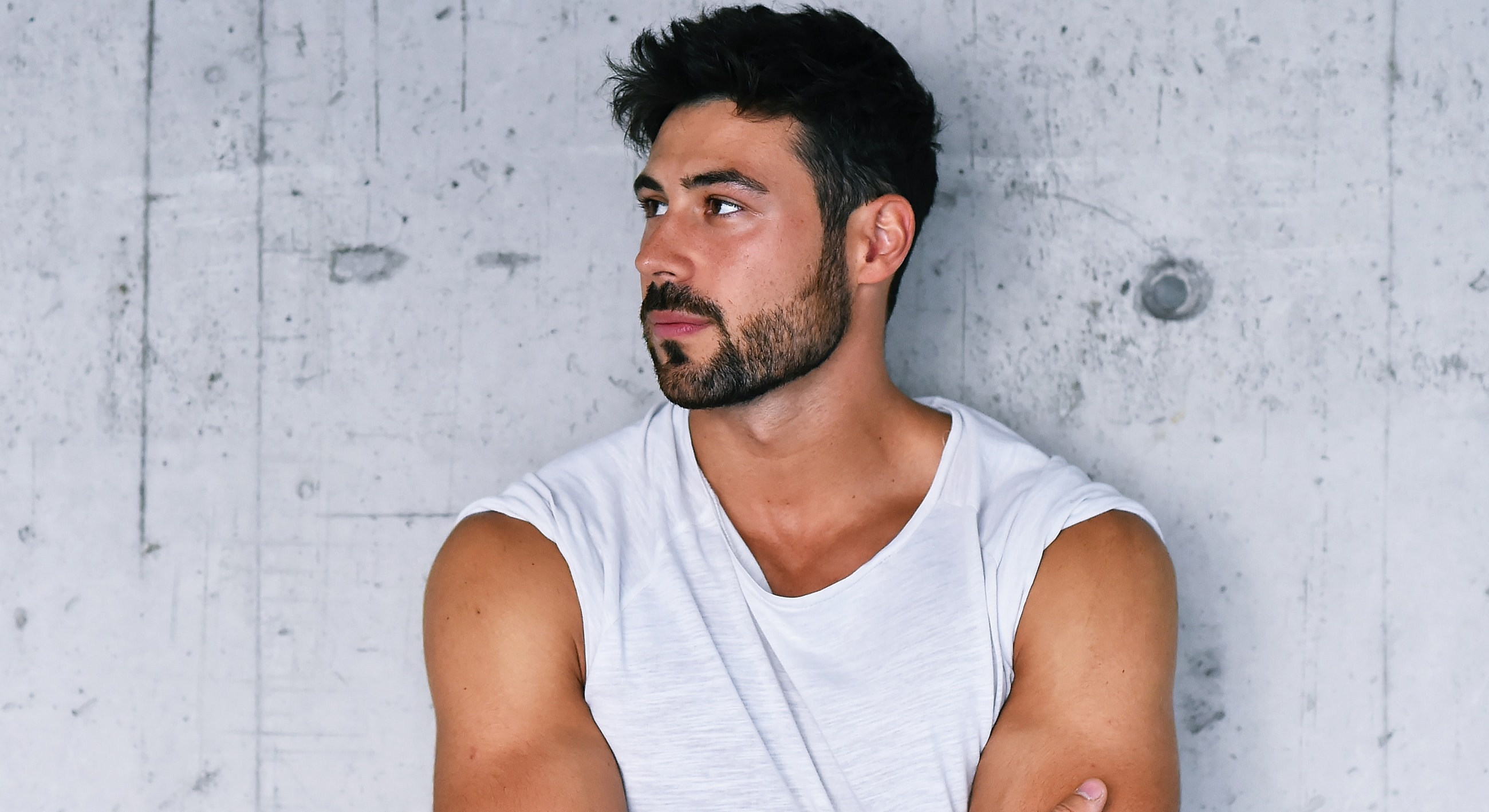 Man with beard posing against a concrete wall.